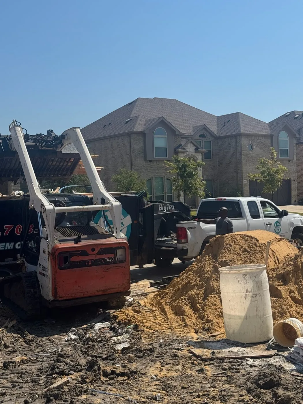 Skid steer loading construction debris into a Daltex trailer at a Dallas-Fort Worth build site