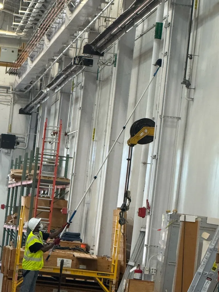 Daltex crew member high dusting overhead pipes and fixtures in a Dallas-Fort Worth industrial facility