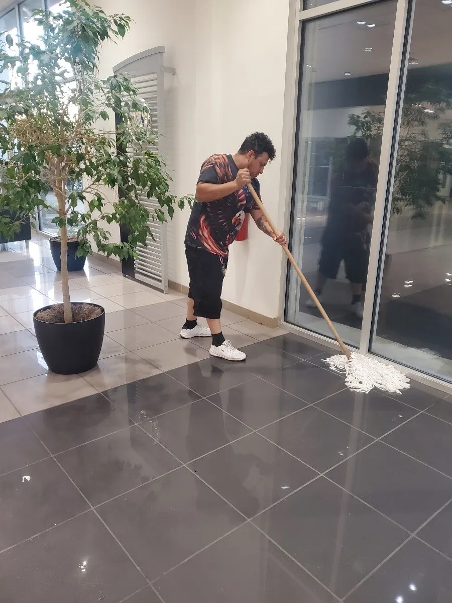Crew member mopping a commercial lobby floor beside entry glass in Dallas-Fort Worth