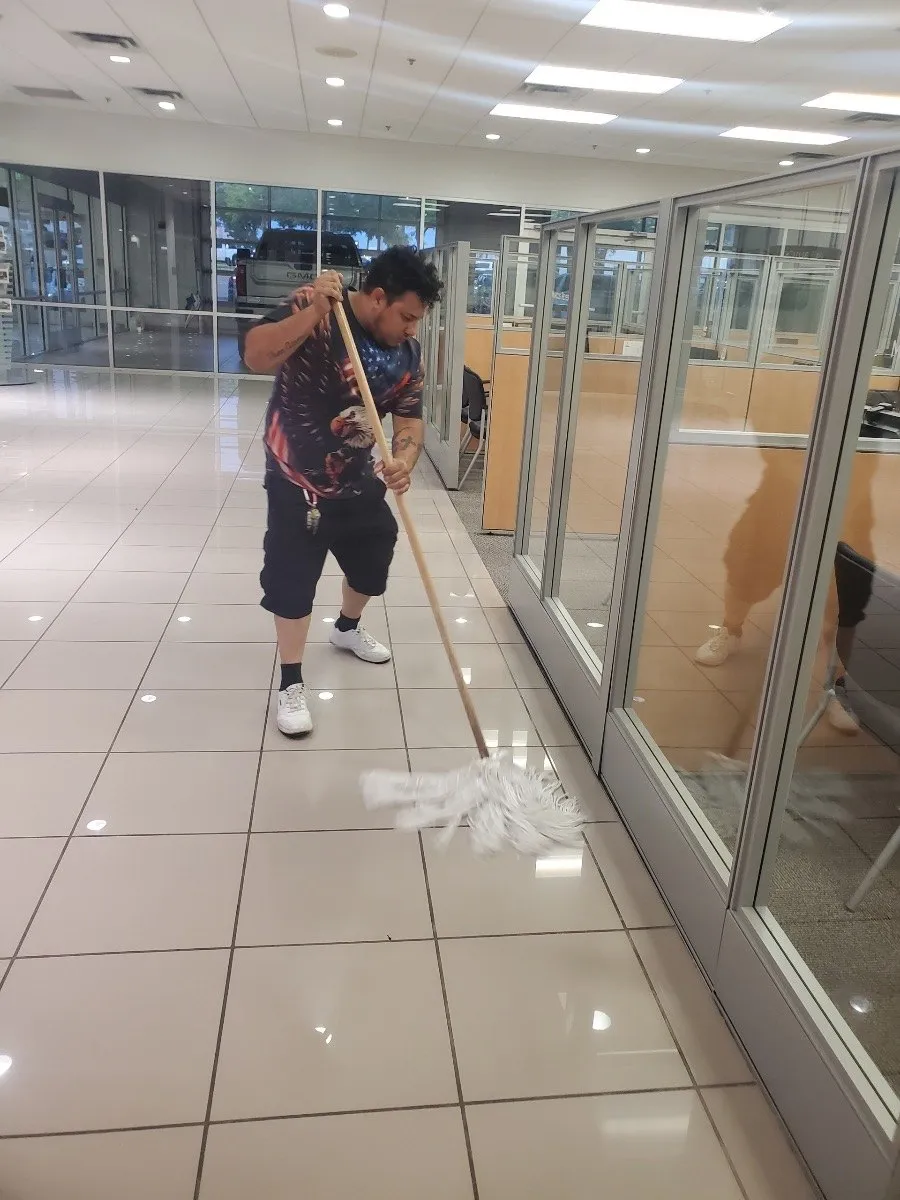 Crew member mopping tile in a Dallas-Fort Worth office corridor beside glass offices